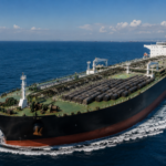 A large oil tanker carries rows of crude barrels across calm blue waters.